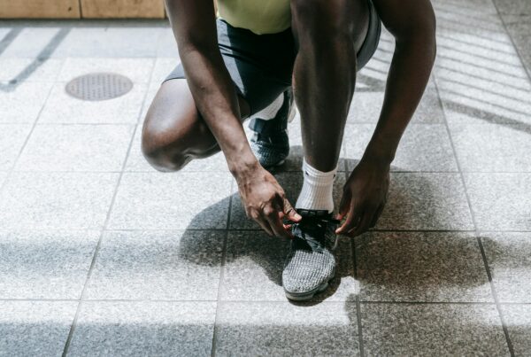 Person kneeling on a tiled floor, tying the laces of a gray athletic shoe with white socks nearby